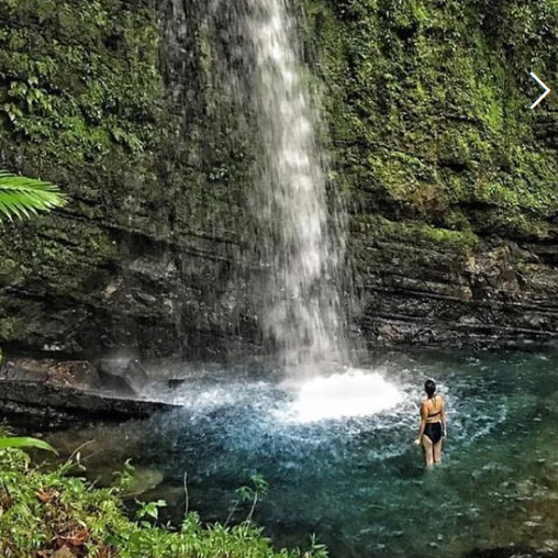 Participant standing under rainforest waterfall in Puerto Rico as part of Root to Rise Retreat adventures