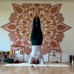 Teresa Prendes-Walls practicing yoga headstand in front of mandala mural at wellness retreat